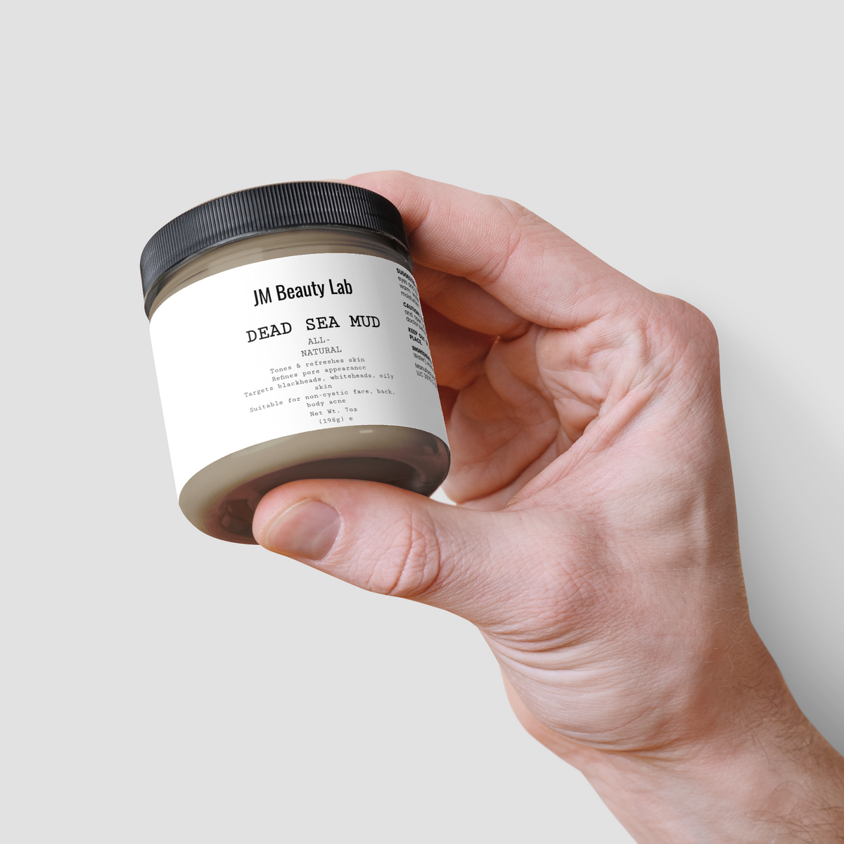 Dead Sea Mud jar angled in hand, showing black lid and front label