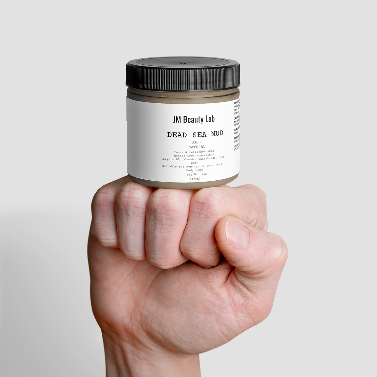 Dead Sea Mud skincare jar held in a hand, black lid and white label