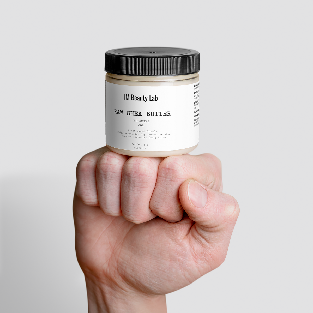 Raw shea butter jar held in hand, black lid and light cream labels visible